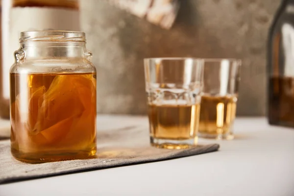 Selective focus of jar with kombucha near glasses on textured grey background — Stock Photo