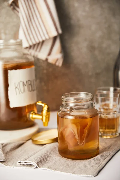 Selective focus of jar with kombucha near glasses on textured grey background with striped napkin — Stock Photo