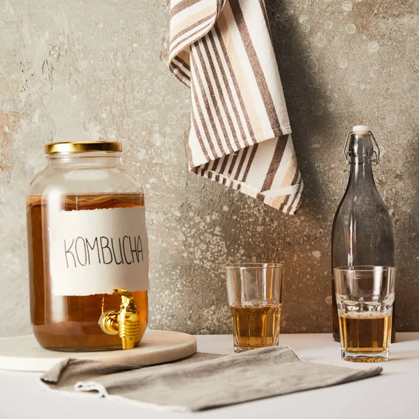 Jar with kombucha near glasses on textured grey background with striped napkin — Stock Photo