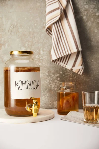 Pot avec kombucha près des lunettes sur fond gris texturé avec serviette rayée — Photo de stock