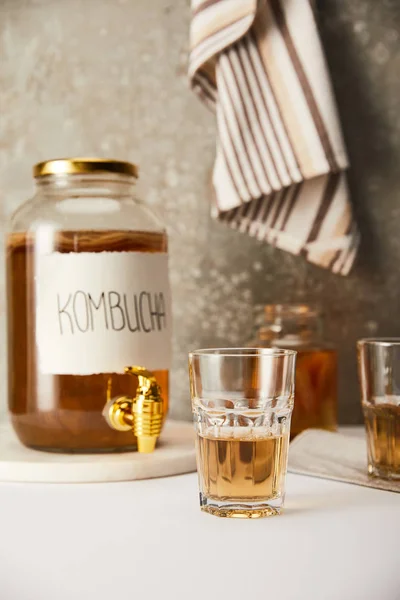 Foyer sélectif de pot avec kombucha près des lunettes sur fond gris texturé avec serviette rayée — Photo de stock