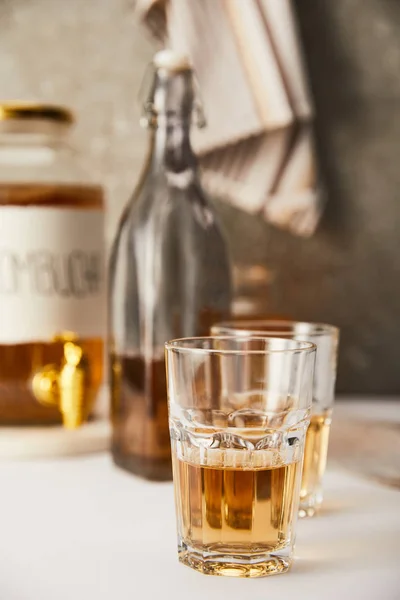 Foyer sélectif de pot avec kombucha près des verres et bouteille sur fond gris texturé avec serviette rayée — Photo de stock