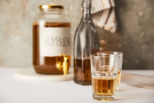Foco seletivo do frasco com kombucha perto de óculos e garrafa em fundo cinza texturizado com guardanapo listrado — Fotografia de Stock