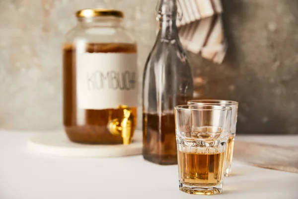 Foyer sélectif de pot avec kombucha près des verres et bouteille sur fond gris texturé avec serviette rayée — Photo de stock