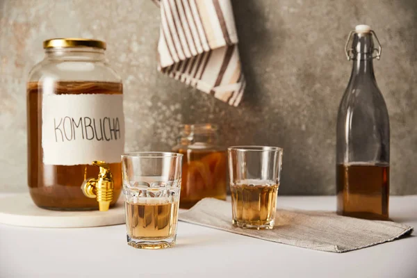 Glas mit Kombucha in der Nähe von Gläsern und Flaschen auf strukturiertem grauen Hintergrund mit gestreifter Serviette — Stockfoto