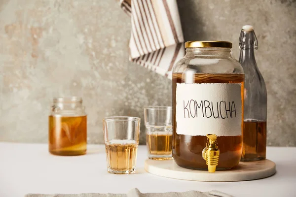 Pot avec kombucha près des verres et bouteille sur fond gris texturé avec serviette rayée — Photo de stock