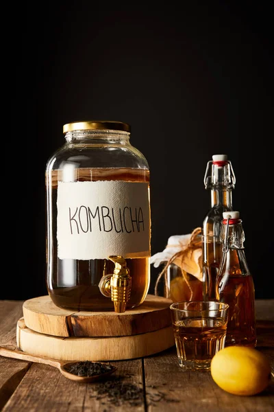 Bocal en verre avec kombucha près de citron, épices et bouteilles sur table en bois isolé sur noir — Photo de stock