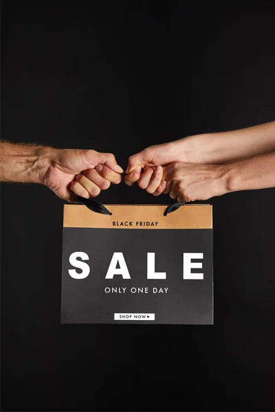 Partial view of woman and man holding paper shopping bag with sale only one day illustration isolated on black, black Friday concept — Stock Photo
