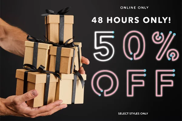 Vista recortada del hombre sosteniendo cajas de regalo de cartón con cintas aisladas en negro con 48 horas 50 por ciento de ilustración, concepto de viernes negro - foto de stock