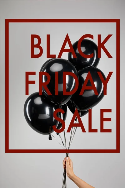 Partial view of woman holding bunch of black balloons isolated on grey with black Friday sale illustration — Stock Photo