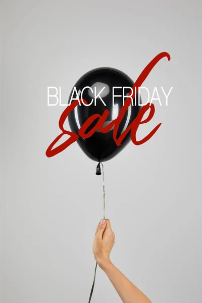 Vista recortada de la mujer sosteniendo globo negro aislado en gris con ilustración de la venta del viernes negro - foto de stock