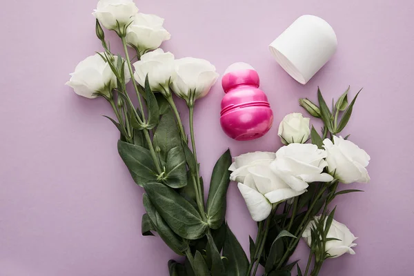 Вид зверху рулону на пляшці дезодоранту на фіолетовому фоні з білими трояндами — стокове фото