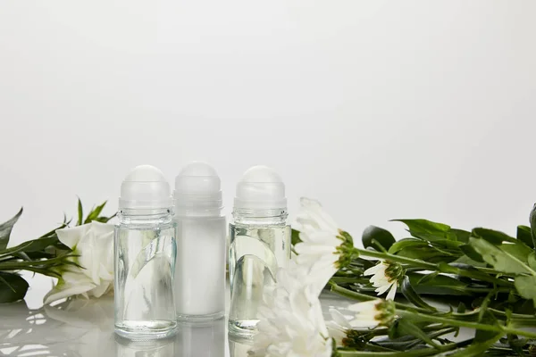 Rolo em garrafas de desodorizante com flores isoladas em branco — Fotografia de Stock