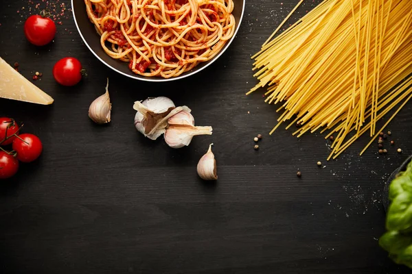 Vue du dessus de savoureuses pâtes bolognaises dans une poêle sur fond noir avec des ingrédients frais — Photo de stock