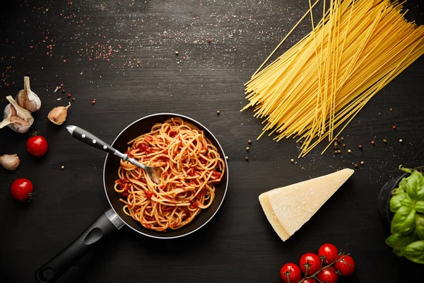 Draufsicht auf leckere Bolognese-Pasta in der Pfanne auf schwarzem Hintergrund mit frischen Zutaten — Stockfoto