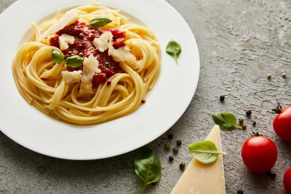 Leckere Bolognese-Pasta mit Tomatensauce und Parmesan auf weißem Teller in der Nähe von Zutaten auf grauem Hintergrund — Stockfoto