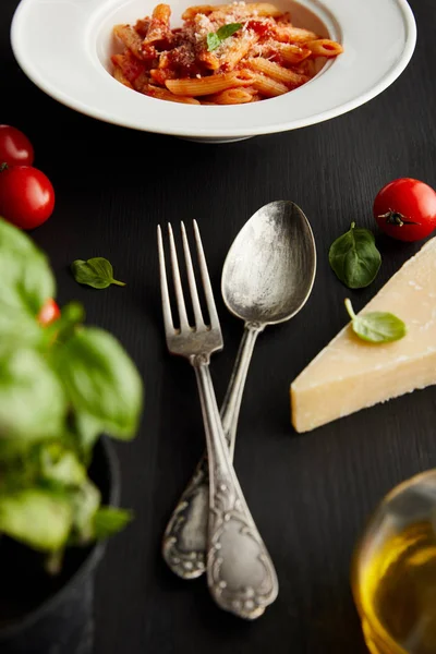 Selective focus of tasty bolognese pasta near ingredients and cutlery on black background — Stock Photo