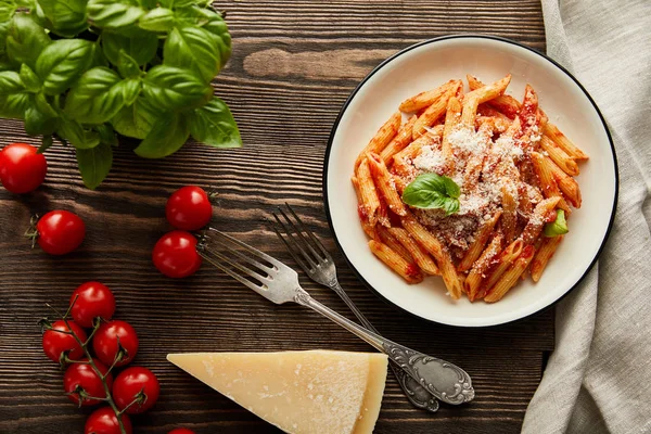 Vista superior de la sabrosa pasta boloñesa con salsa de tomate y parmesano en plato blanco cerca de los ingredientes y cubiertos en la mesa de madera - foto de stock