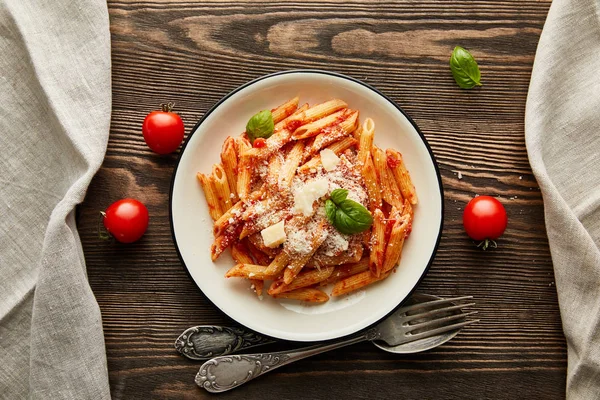 Вид на вкусные болоньезе макароны с томатным соусом и пармезан в белой тарелке рядом с ингредиентами и столовыми приборами на деревянном столе — стоковое фото