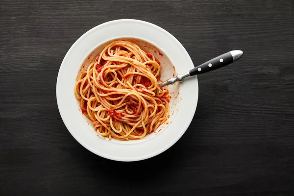 Верхний вид вкусной болоньезе пасты с томатным соусом в белой тарелке на черном деревянном фоне — стоковое фото