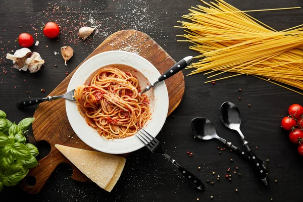 Vista dall'alto della gustosa pasta bolognese in piatto bianco vicino agli ingredienti e posate su fondo nero in legno — Foto stock