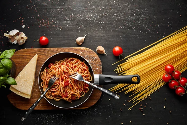 Vista dall'alto della gustosa pasta bolognese in padella vicino agli ingredienti e posate su fondo di legno nero — Foto stock