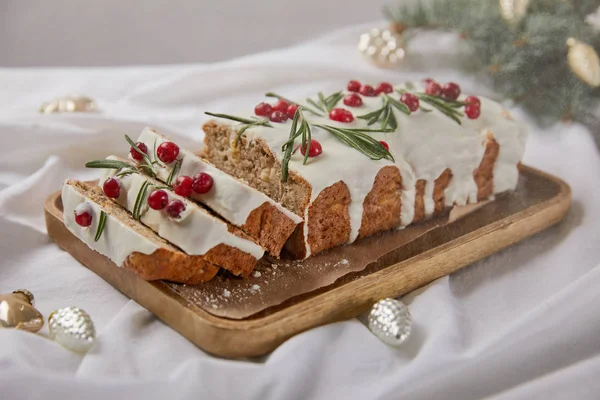 Traditional Christmas cake with cranberry on wooden board near silver baubles and pine needles isolated on grey with falling snow — Stock Photo