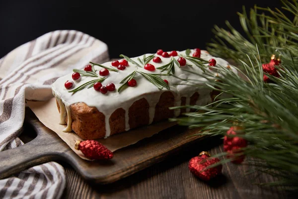 Traditional Christmas cake with cranberry near pine and baubles on wooden table isolated on black — Stock Photo