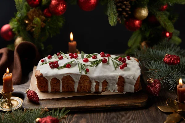 Traditional Christmas cake with cranberry near Christmas wreath with baubles and candles on wooden table isolated on black — Stock Photo