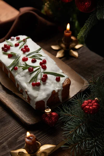 Традиционный рождественский торт с клюквой возле сосны с безделушками и свечами на деревянном столе — стоковое фото