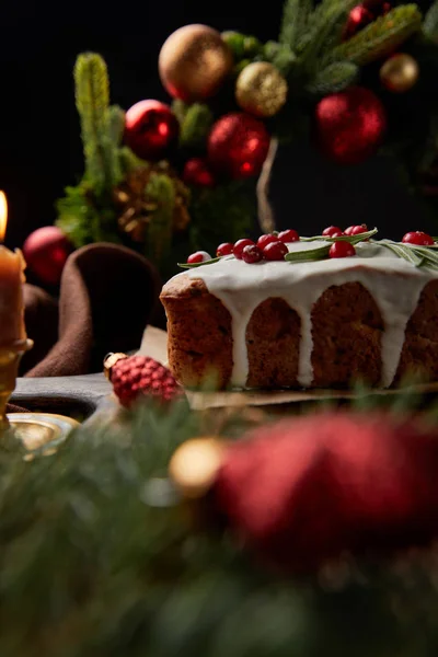 Selective focus of traditional Christmas cake with cranberry near Christmas wreath with baubles on wooden table isolated on black — Stock Photo