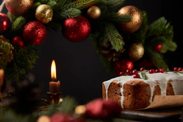 Bolo de Natal tradicional com cranberry perto da grinalda de Natal com bugigangas e vela na mesa de madeira isolada em preto — Fotografia de Stock