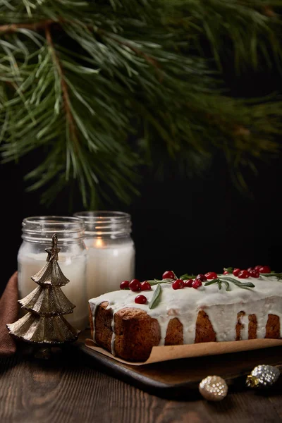 Traditional Christmas cake with cranberry near pine, baubles and candles on wooden table — Stock Photo
