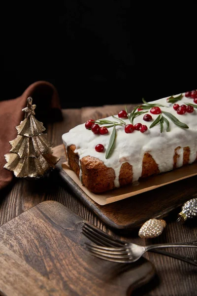 Pastel tradicional de Navidad con arándano cerca de bolas, tenedores y servilleta marrón en la mesa de madera aislado en negro - foto de stock