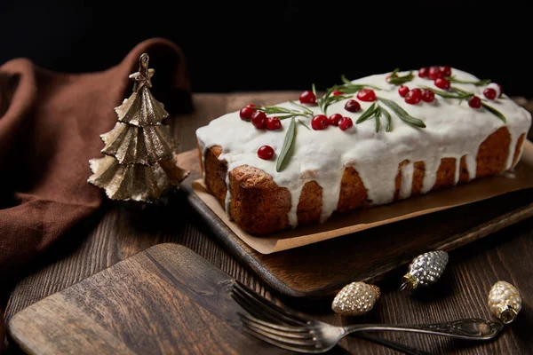 Traditional Christmas cake with cranberry near baubles, forks and brown napkin on wooden table isolated on black — Stock Photo