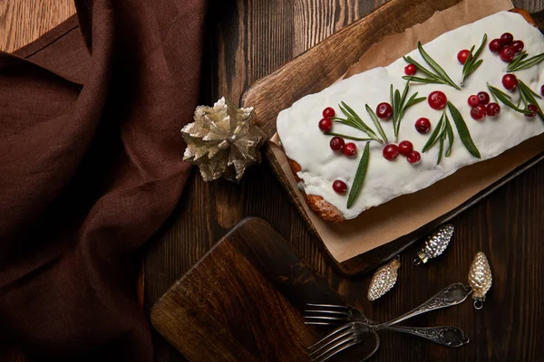 Draufsicht auf traditionellen Weihnachtskuchen mit Preiselbeeren in der Nähe von Christbaumkugeln, Gabel und brauner Serviette auf Holztisch — Stockfoto