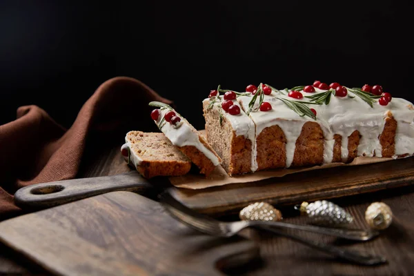 Traditional Christmas cake with cranberry near baubles, fork and brown napkin on wooden table isolated on black — Stock Photo