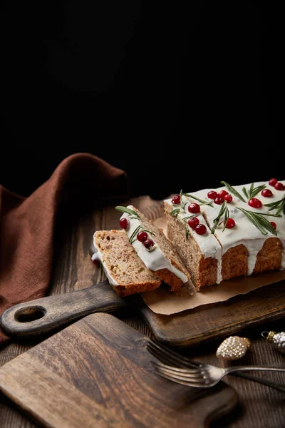 Gâteau de Noël traditionnel avec canneberge près de boules, fourchette et serviette brune sur table en bois isolé sur noir — Photo de stock