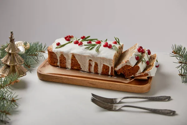 Traditioneller Weihnachtskuchen mit Preiselbeeren in der Nähe von Gabeln, Kugeln und Kiefern auf weißem Tisch isoliert auf grau — Stockfoto