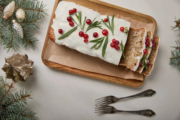 Vista superior do bolo de Natal tradicional com cranberry perto de garfos, bugigangas e pinheiros na mesa branca — Fotografia de Stock
