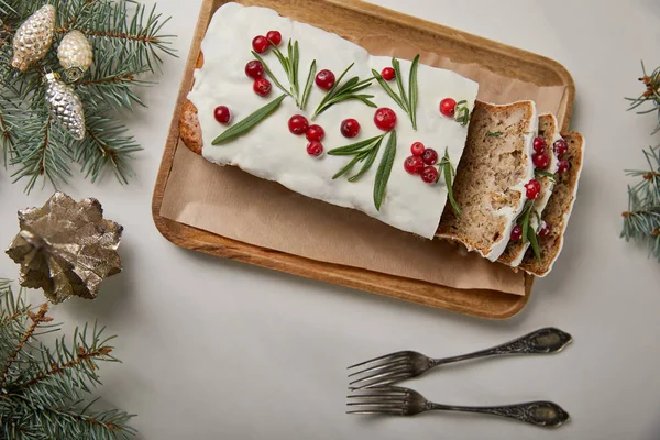 Vista superior de la torta tradicional de Navidad con arándano cerca de tenedores, bolas y pino en la mesa blanca - foto de stock