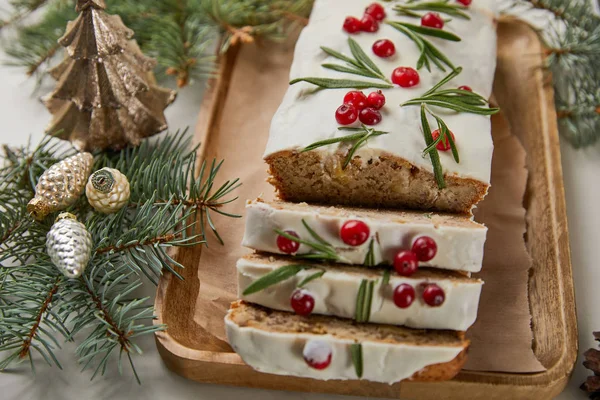 Traditioneller Weihnachtskuchen mit Preiselbeeren in der Nähe von Christbaumkugeln und Kiefern auf weißem Tisch — Stockfoto