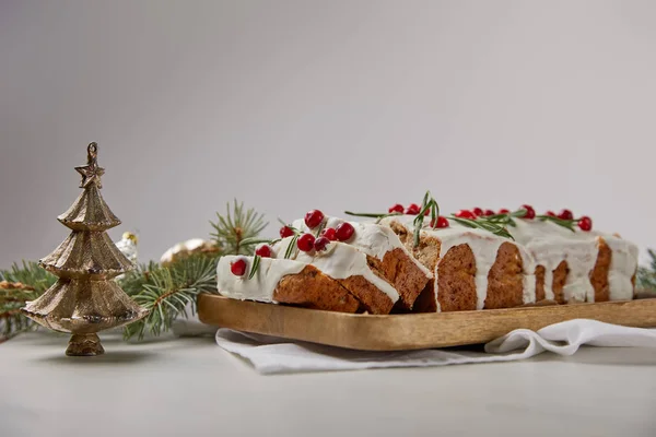 Традиционный рождественский торт с клюквой возле безделушки и сосны на мраморном столе, изолированном на сером — стоковое фото