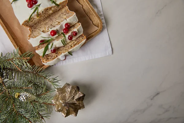 Draufsicht auf traditionellen Weihnachtskuchen mit Preiselbeere in der Nähe von Christbaumkugel und Kiefer auf Marmortisch — Stockfoto