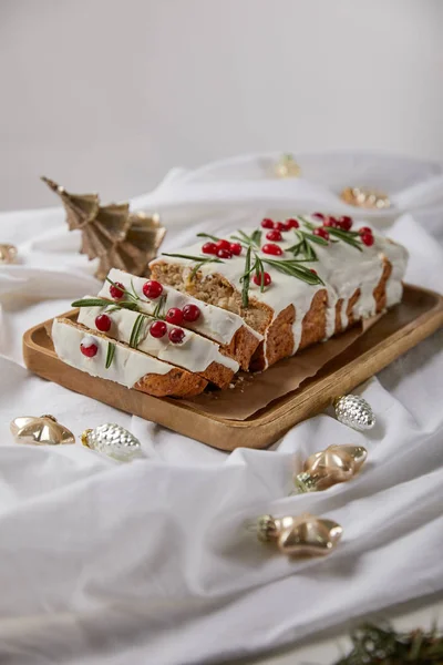 Traditioneller Weihnachtskuchen mit Preiselbeeren auf Holzbrett in der Nähe von Kugeln auf weißem Tuch isoliert auf grau — Stockfoto