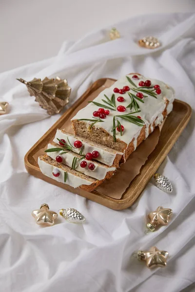 Traditional Christmas cake with cranberry on wooden board near baubles on white cloth isolated on grey — Stock Photo