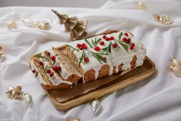 Traditional Christmas cake with cranberry on wooden board near baubles on white cloth — Stock Photo