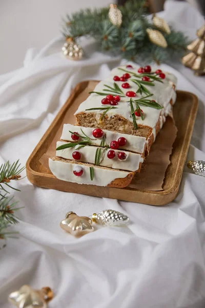 Selektiver Schwerpunkt des traditionellen Weihnachtskuchens mit Preiselbeere auf Holzbrett in der Nähe von Kugeln und Kiefer auf weißem Tuch isoliert auf grau — Stockfoto