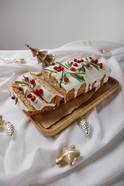 Traditional Christmas cake with cranberry on wooden board near baubles on white cloth isolated on grey — Stock Photo