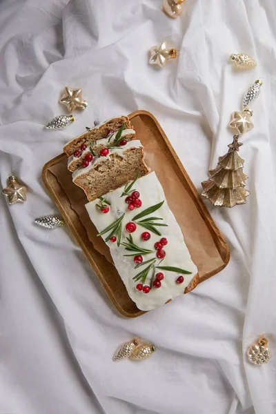 Top view of traditional Christmas cake with cranberry on wooden board near baubles on white cloth — Stock Photo